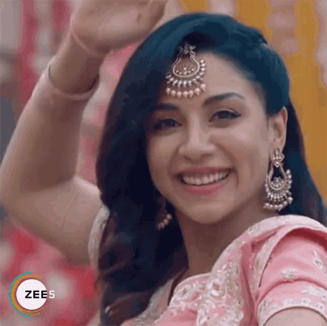 a woman wearing a pink dress and earrings is smiling and waving .