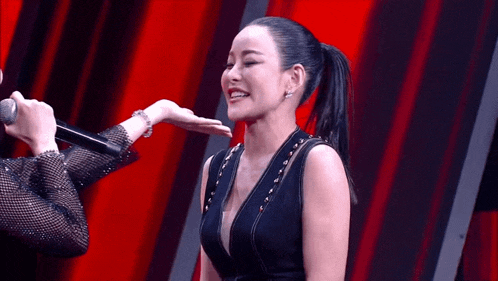 a woman in a black dress is smiling while another woman holds her hand to her face
