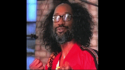 a man with long curly hair and a beard wearing glasses and a red shirt .