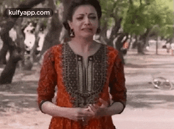 a woman in a red dress is standing in a park with trees in the background .
