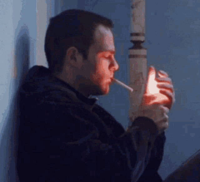a man is smoking a cigarette in front of a blue wall .
