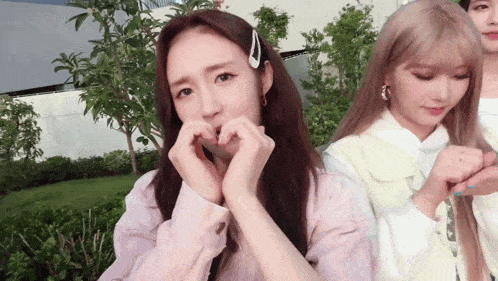 a girl making a heart with her hands while another girl looks on