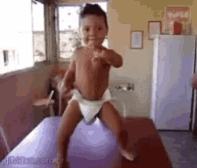 a baby in a diaper is standing on a table giving a thumbs up .