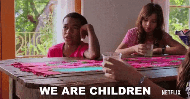 a group of children are sitting at a table and a person is holding a cup of milk and saying we are children .