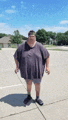 a very fat man is standing on a sidewalk wearing shorts and a t-shirt .