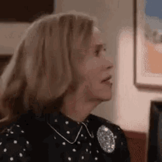 a woman in a black and white polka dot dress is sitting on a couch and making a funny face .