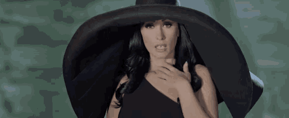 a woman wearing a black hat and a black dress is standing in front of a green background .