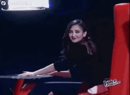 a woman is smiling while sitting in a red chair on a stage .