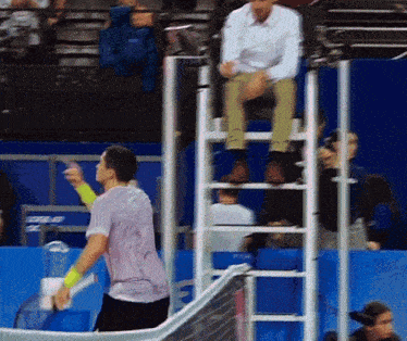 a man in a purple shirt holds a tennis racquet in front of a referee