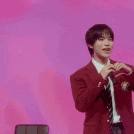 a man in a red suit and tie is making a heart with his hands .