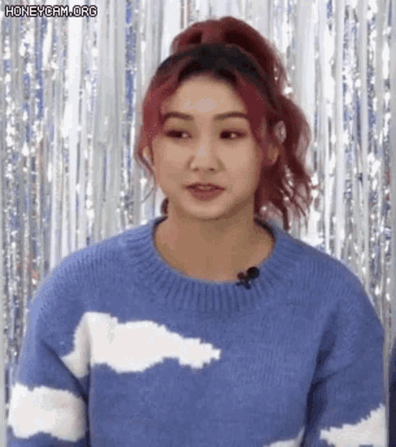 a woman with red hair is wearing a blue sweater with white clouds and a microphone .