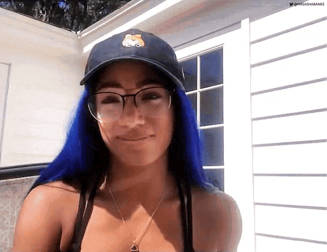 a woman with blue hair and glasses is wearing a hat and necklace .