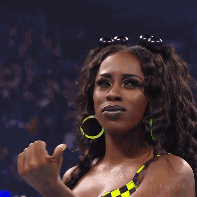 a woman wearing a yellow and black checkered top and green hoop earrings has the number 24 on her chest