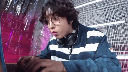a man wearing glasses and headphones is typing on a laptop computer .
