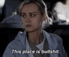 a woman is sitting at a table in a dark room and saying `` this place is bullshit '' .