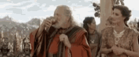 a man in a red robe is drinking a glass of wine while standing next to a woman .