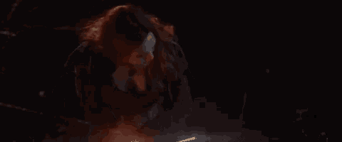 scarlet witch is wearing a black jacket and a necklace in a dark room .