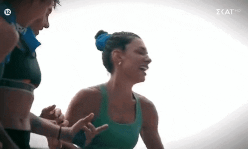 a woman in a green tank top is laughing while standing next to a man in a black top .