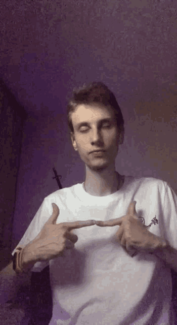 a young man in a white t-shirt is pointing at himself .