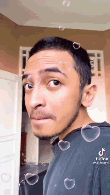 a man with heart shaped soap bubbles around his head is wearing a black shirt that says tiktok