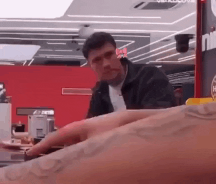 a man in a black jacket is sitting at a table in a restaurant with a tattoo on his arm .