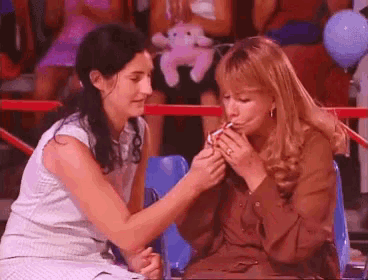 two women are sitting next to each other and one of them is smoking a cigarette .