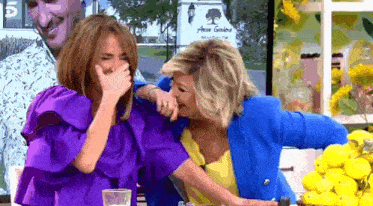 a woman in a purple top is covering her mouth while another woman in a blue jacket laughs .