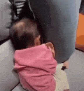 a baby in a pink shirt is laying on a couch with his head on a pillow .