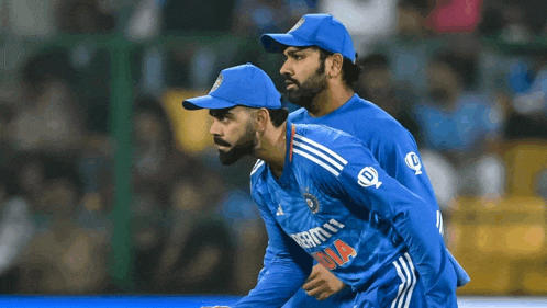two cricket players wearing blue uniforms with the letter d on the front