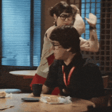 a man wearing glasses is sitting at a table with a woman behind him