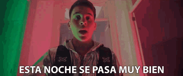 a young man is standing in a dark room with his mouth open and the words esta noche se pasa muy bien written on the bottom .