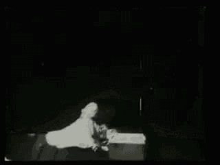 a black and white photo of a man laying on a bed in a dark room .