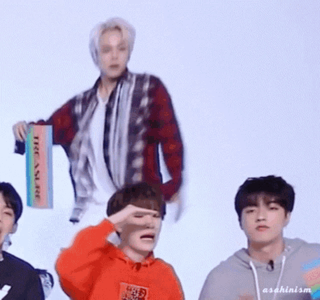 a group of young men are standing next to each other and one of them is wearing an orange hoodie .