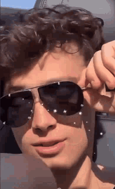 a young man with curly hair is wearing sunglasses and making a funny face .