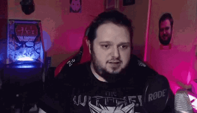 a man with a beard is sitting in front of a microphone in a room with purple lights .