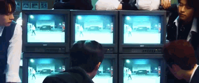 a group of young men are sitting in front of a stack of televisions .