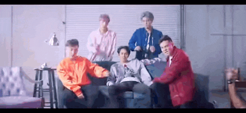 a group of young men are standing around a couch .
