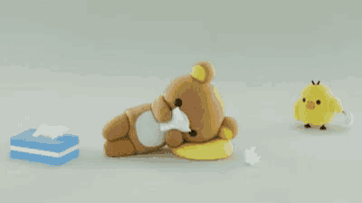 a teddy bear is laying on a pillow next to a box of tissues .