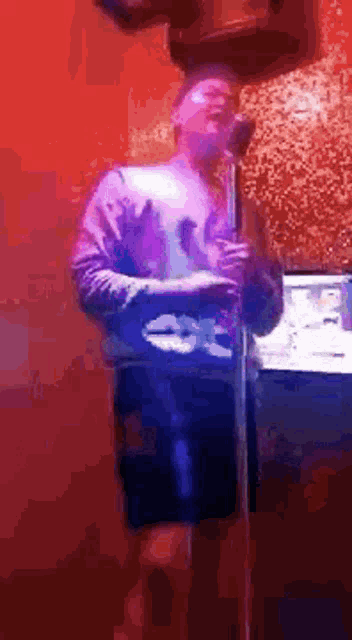 a man is singing into a microphone while standing in front of a red wall .