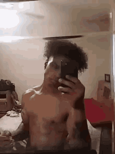 a shirtless man is taking a selfie in a bedroom .