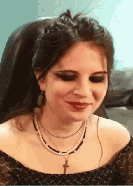 a woman wearing a necklace with a cross on it is sitting in a chair .