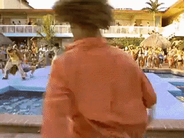 a man in an orange shirt is standing in front of a swimming pool