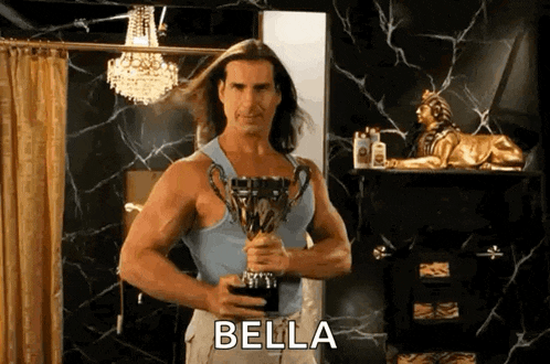 a man in a blue tank top is holding a trophy in a bathroom and says bella .
