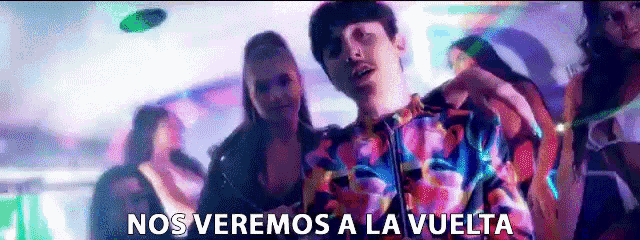 a man in a colorful shirt is standing in front of a crowd with the words nos veremos a la vuelta above him