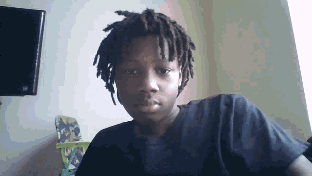 a young boy with dreadlocks wearing a black shirt looks at the camera