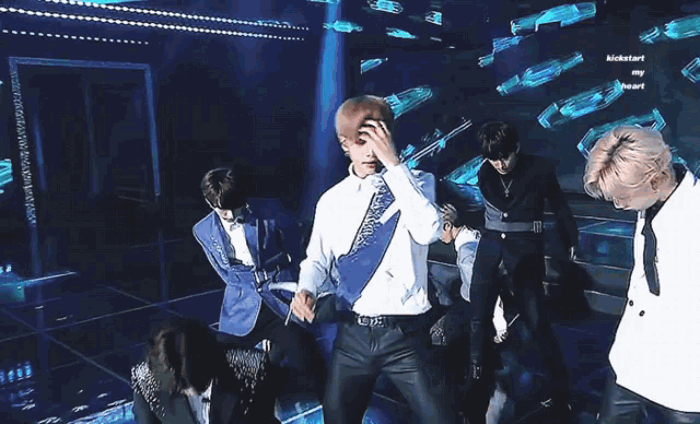 a man in a white shirt and blue vest is dancing on a stage in front of a screen that says kickstart my heart