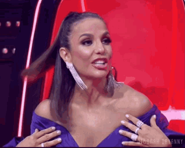 a woman in a purple dress is sitting in a red chair with her hands on her breasts .