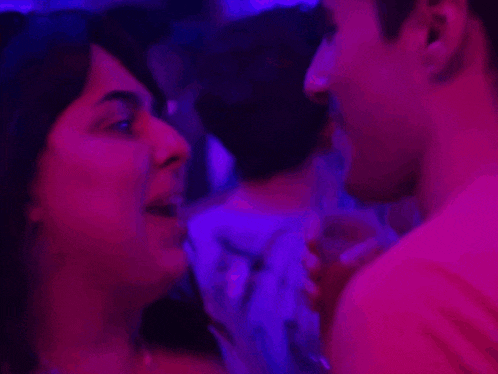 a man in a pink shirt is smiling in a purple light