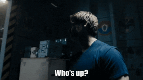 a man in a blue shirt says " who 's up " in a dark room