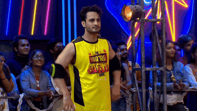 a man wearing a yellow shirt that says ' what tru ' on it is standing in front of a crowd of people